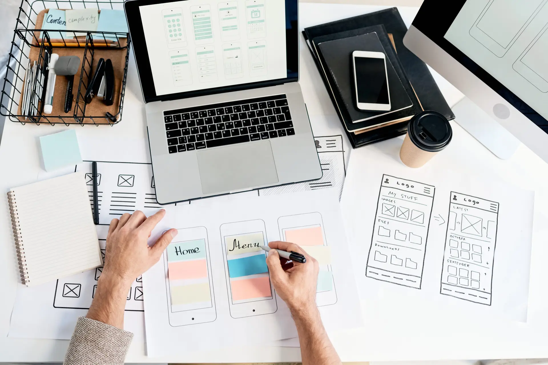 Designer creating mobile-app wireframes on paper while referencing digital mock-ups on a laptop—UI/UX workflow at W3Inventor