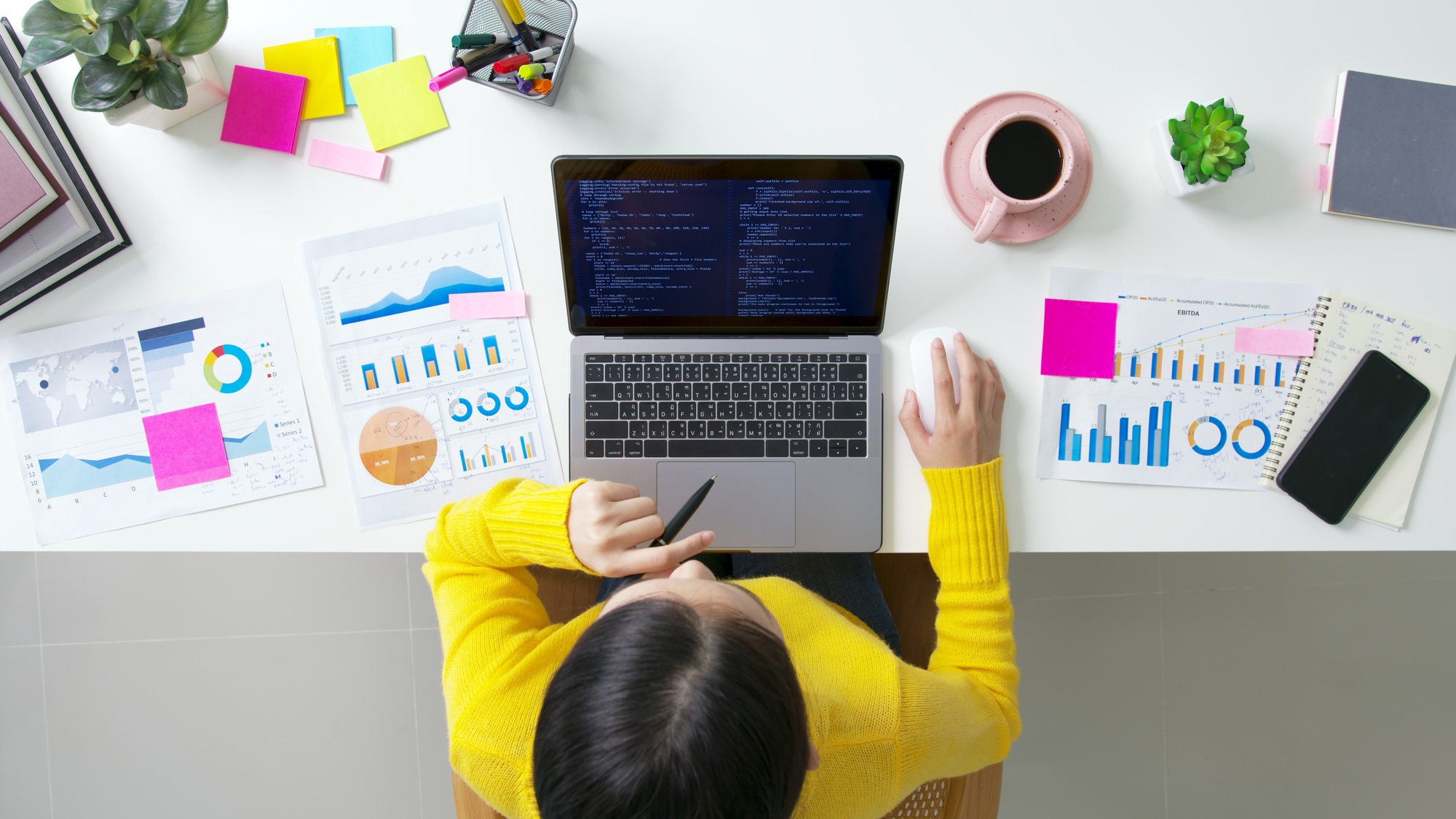 Top view of a developer analyzing digital transformation KPIs with charts, code, and strategy notes on desk